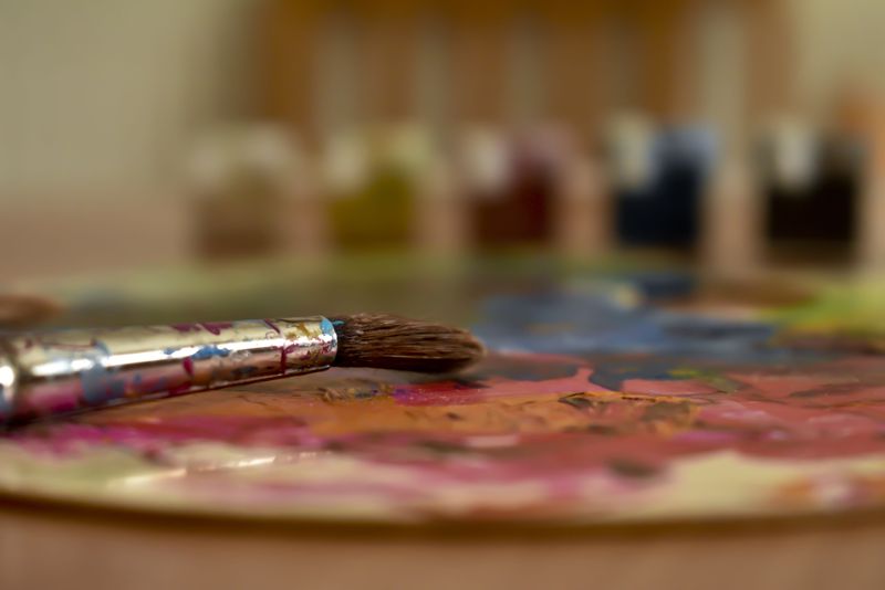 Well-used paintbrush resting on a palette covered in mixed colors